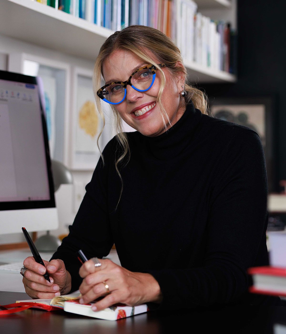 Patricia Tempski sorrindo em seu escritório, com um caderno e uma caneta nas mãos